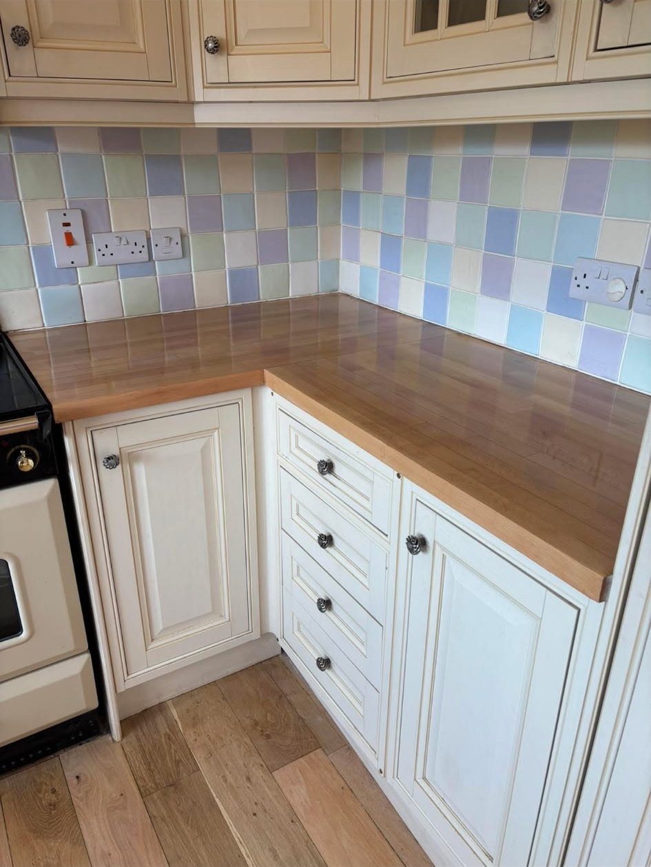 Restored wooden kitchen worktop in a corner, with cream cabinets