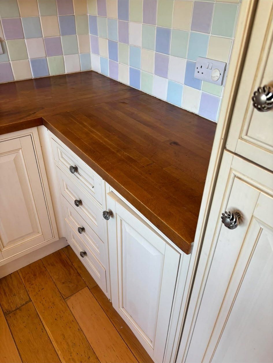 Restored wooden kitchen worktop beside cream cabinets and pastel tiles